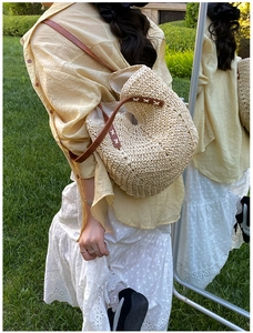 Close-up of beige woven straw tote featuring brown leather straps and cross-stitch detail