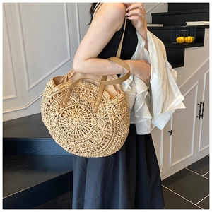 Detail of hand-woven straw tote bag showing radial texture and brown PU leather shoulder straps
