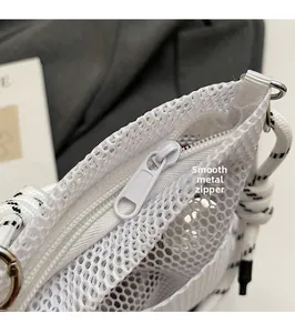 Detail of smooth white metal zipper head and fine woven strap on a mesh crossbody bag