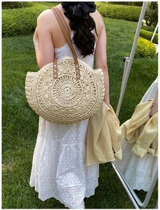 Detail of round straw beach bag with spiral woven pattern and brown leather strap