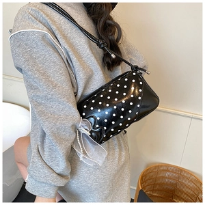 Close-up of black polka dot bag with white tulle bow and pearl charms on a model