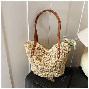 Detail of hand-woven straw tote bag with brown leather handles and decorative white stitching