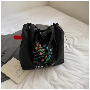 Close-up of black canvas tote bag featuring floral embroidery and tea me letter print