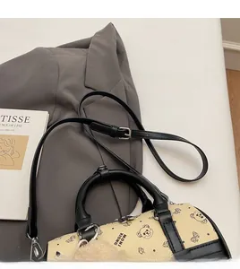 Close-up of beige Boston bag with bear print, black handles and adjustable strap