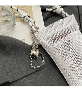 Detail of white mesh phone bag with silver heart charm and woven strap on grey background