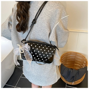 Detail of black polka dot bag with translucent bow and pearl charm on a model