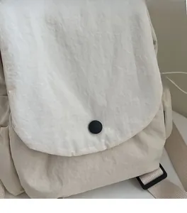 Detail of off-white canvas backpack featuring a front flap and round black button closure