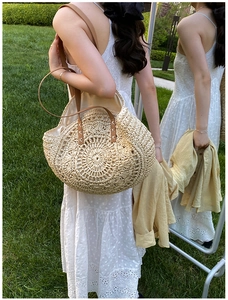 Detail of handwoven circular straw tote bag with brown leather handles and cross-stitching