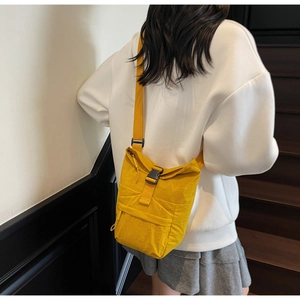Detalle del bolso bandolera de nailon amarillo jengibre con hebilla negra llevado por una modelo