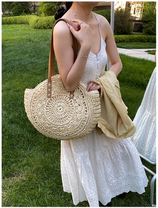 Detailed close-up of woven straw shoulder bag with elegant brown leather strap attachments