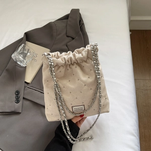 Detail of beige quilted bucket bag with silver studs, chain strap and drawstring closure
