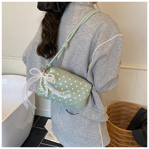 Detail of light green polka dot baguette bag featuring pearl chain and ribbon bow