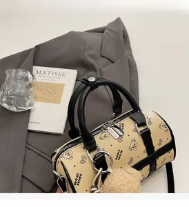 Detail of beige boston bag with bear print, leather handles and plush bear charm
