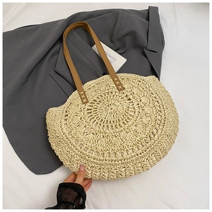Detailed macro view of woven straw tote bag with brown leather handles and metal rivets