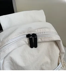Close-up of dual black zippers on a cream nylon backpack showing smooth hardware detail