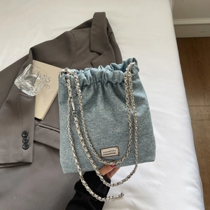 Detail of light blue denim bucket bag with rhinestone decor and silver chain straps
