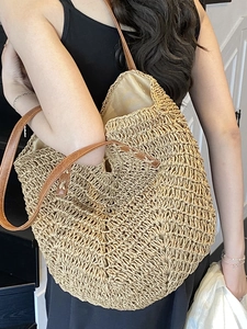 Large straw tote bag with brown leather straps shown on model for beach vacations