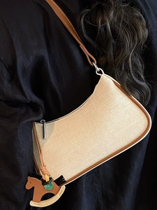 Chic beige woven hobo bag with brown leather trim and horse charm on black background