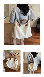 Detail of white canvas tote bag featuring brown leather handles and artful typography