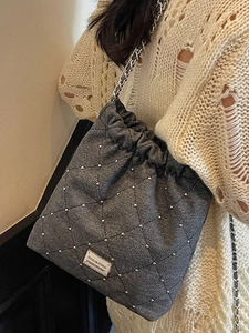 Gray quilted bucket bag with silver studs and metal chain strap shown on shoulder