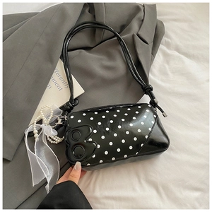 Detailed view of black polka dot bag with letter B emblem and pearl bow charm