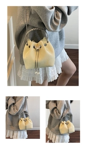 Detail of light yellow suede bucket bag with silver woven handle and butterfly charm