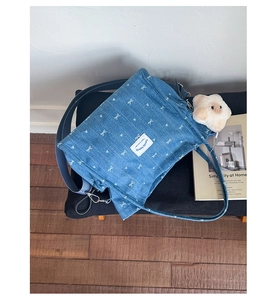Detail of blue denim tote bag with white bow print and cute plush charm hanging on the side