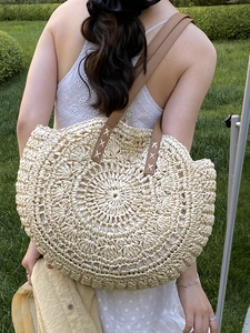 Straw beach tote bag with leather handles shown in a natural outdoor summer setting