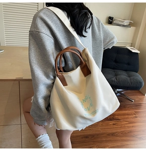 Minimalist cream canvas tote bag with brown leather handles worn by a model in interior