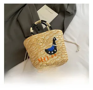 Detail of handmade straw tote bag featuring embroidered duck pattern and rope handle