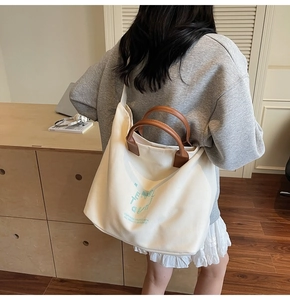 Detail of canvas tote bag showing brown leather handles and adjustable shoulder strap