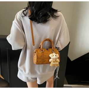 Detail view of brown barrel-shaped bag with cartoon bear pattern and plush bear charm