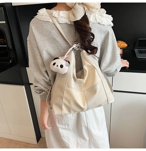 Close-up of a cream-white tote bag featuring a cute panda plush charm and textured leather