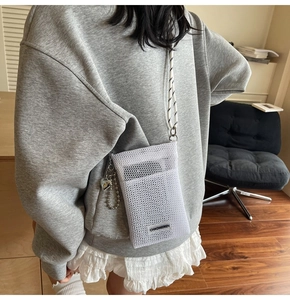 Detail of white mesh phone bag with silver heart charm and woven crossbody strap