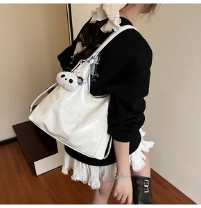 Detail of white glossy tote bag with detachable panda plush charm and wide strap