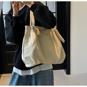 Detail view of beige tote bag showing the stylish knotted shoulder strap design and material