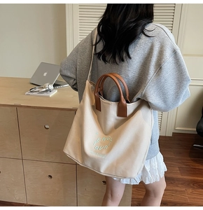Close-up of beige canvas tote with brown leather straps and green text print
