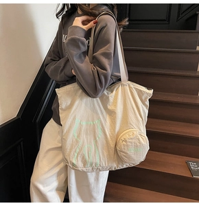 Detail of off-white tote bag with green cat line print and a small round coin purse charm