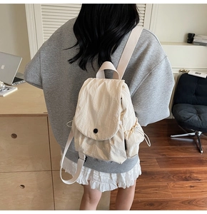 Detail of a creamy white canvas backpack with drawstring side pockets and flap closure