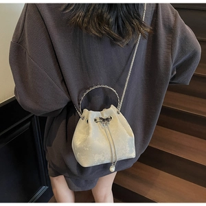 Detail view of pearl white drawstring bucket bag with metal handle and butterfly charm