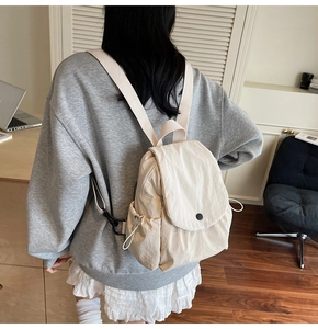 Detail of minimalist cream canvas backpack with flap closure and side drawstring pocket