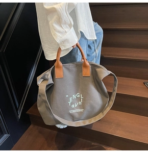 Detail of grey canvas tote bag with brown leather handles on wooden stairs