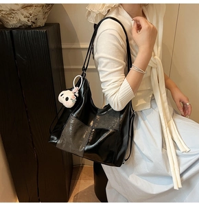 Detail of glossy black leather tote bag featuring a cute white panda plush pendant charm