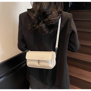 Detail shot of a beige leather baguette bag with PARIS embossing on a black blazer