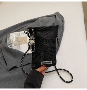 Detail of black mesh crossbody phone bag with woven strap and heart charm on grey blazer