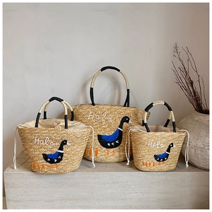 Detail view of woven straw basket bags with duck embroidery and contrast handles