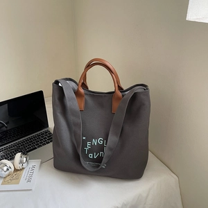 Detail of grey canvas tote bag with brown leather handles and notebook accessories