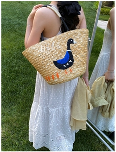 Detailed close-up of straw tote bag featuring blue duck embroidery and Hala lettering