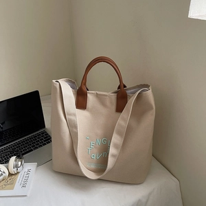 Detail of beige canvas tote bag with green embroidery and premium brown leather handles