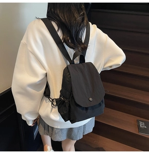 Rear view of minimalist black canvas backpack with flap cover and drawstring detail on stairs